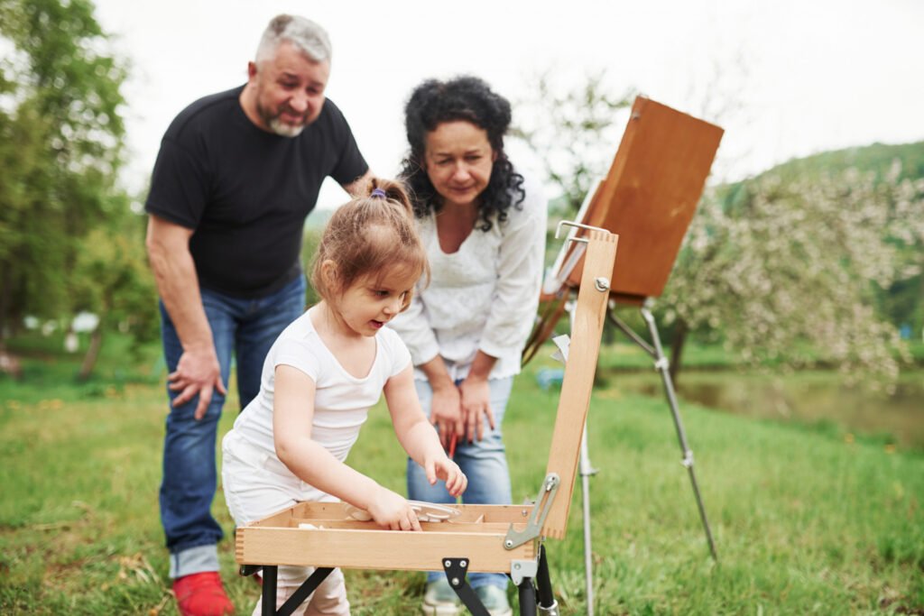 Grandparents and a child painting at an easel outdoors
